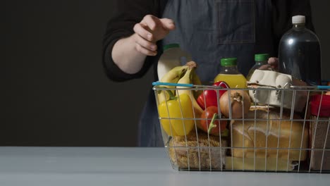 Studio-Shot-Of-Shop-Worker-Checking-Basic-Food-Items-In-Supermarket-Wire-Shopping-Basket-With-Copy-Space