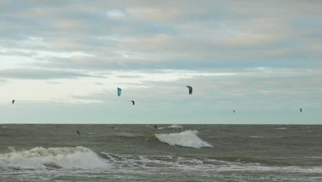 A group of people engaged in kitesurfing in sunny autumn day, high waves, Baltic Sea Karosta beach in Liepaja, wide shot