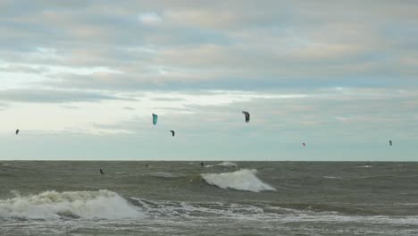 a group of people engaged in kitesurfing in sunny autumn day, high waves, baltic sea karosta beach in liepaja, wide shot