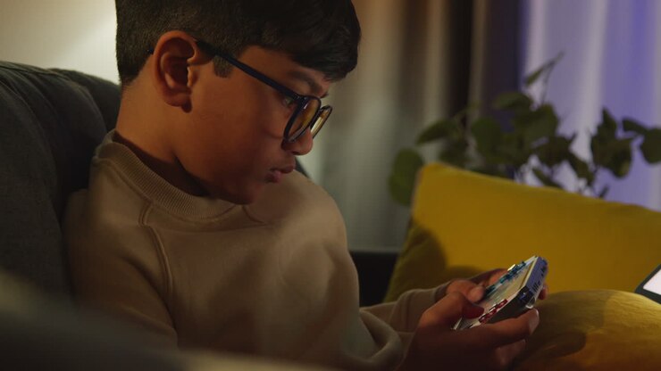 Ragazzo giovane seduto sul divano a casa che gioca o guarda in streaming su un dispositivo di gioco portatile di notte 4