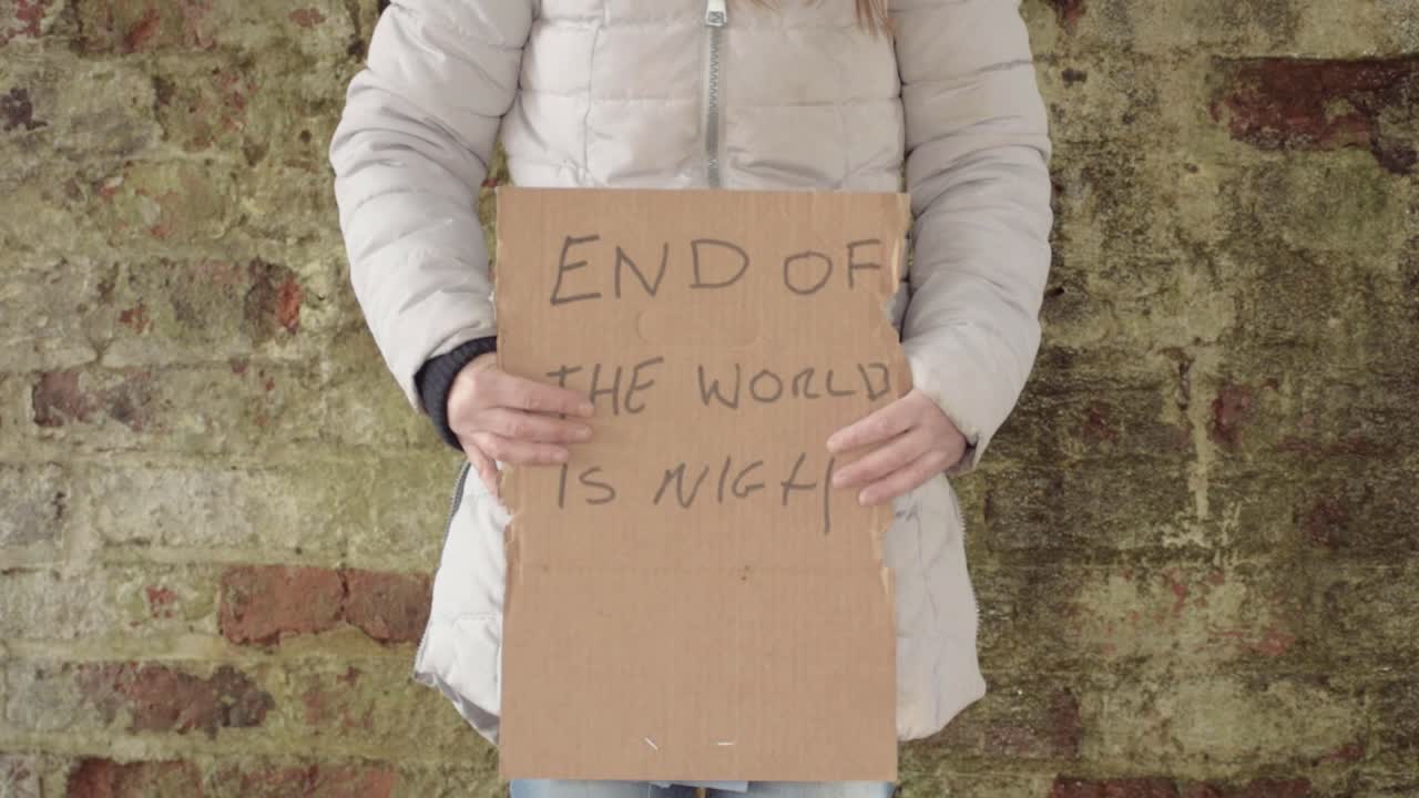 Person holding sign warning of the end of world on dirty brick wall background