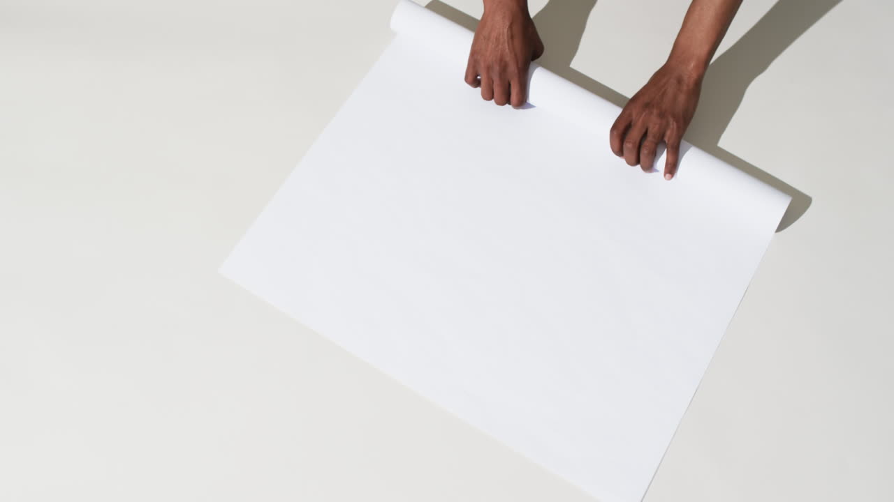 Video delle mani di un uomo afroamericano che arrotola carta bianca su sfondo bianco