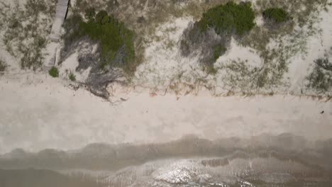 Waves-breaking-along-beach-shoreline-tracking-aerial-overhead-shot