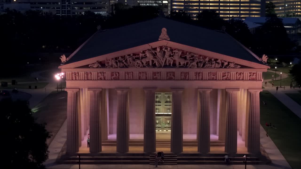 Aerial view of the full scale Parthenon replica in Nashville, Tennessee, glowing warmly against the darkened city backdrop. Rising Shot