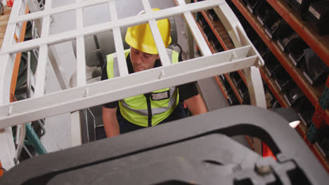 caucasian male factory worker at a factory with a hat and high vis vest, using a truck