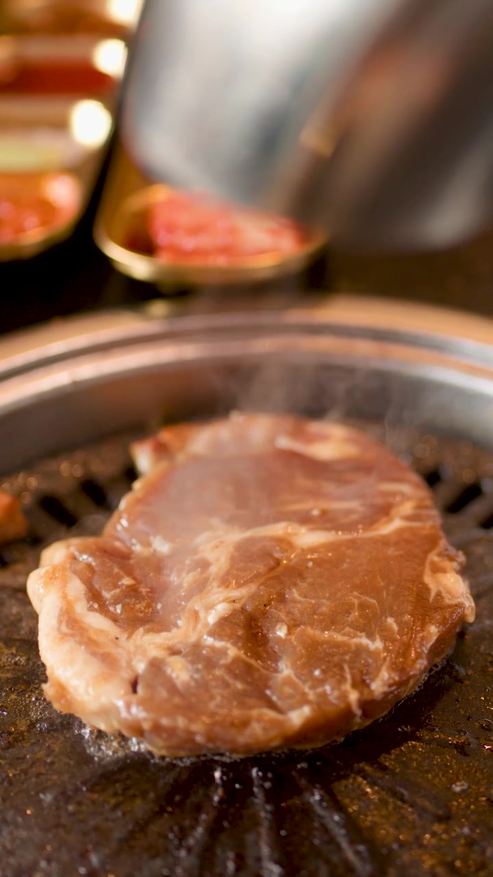 Steak babi mentah dimasak di atas panggangan meja, uap mengepul, pencahayaan hangat, kedalaman bidang dangkal.