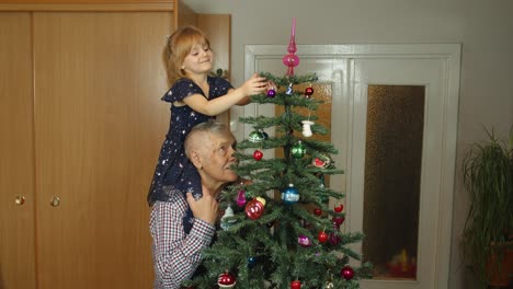 Children-girl-with-elderly-grandparent-decorating-artificial-Christmas-pine-tree-at-old-fashion-home