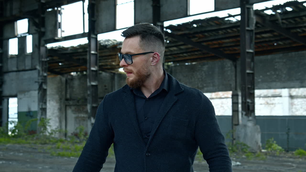 Elegant man with a baseball bat outdoors. Portrait of a serious man in stylish glasses on the background of abandoned building.