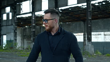 elegant man with a baseball bat outdoors. portrait of a serious man in stylish glasses on the background of abandoned building.