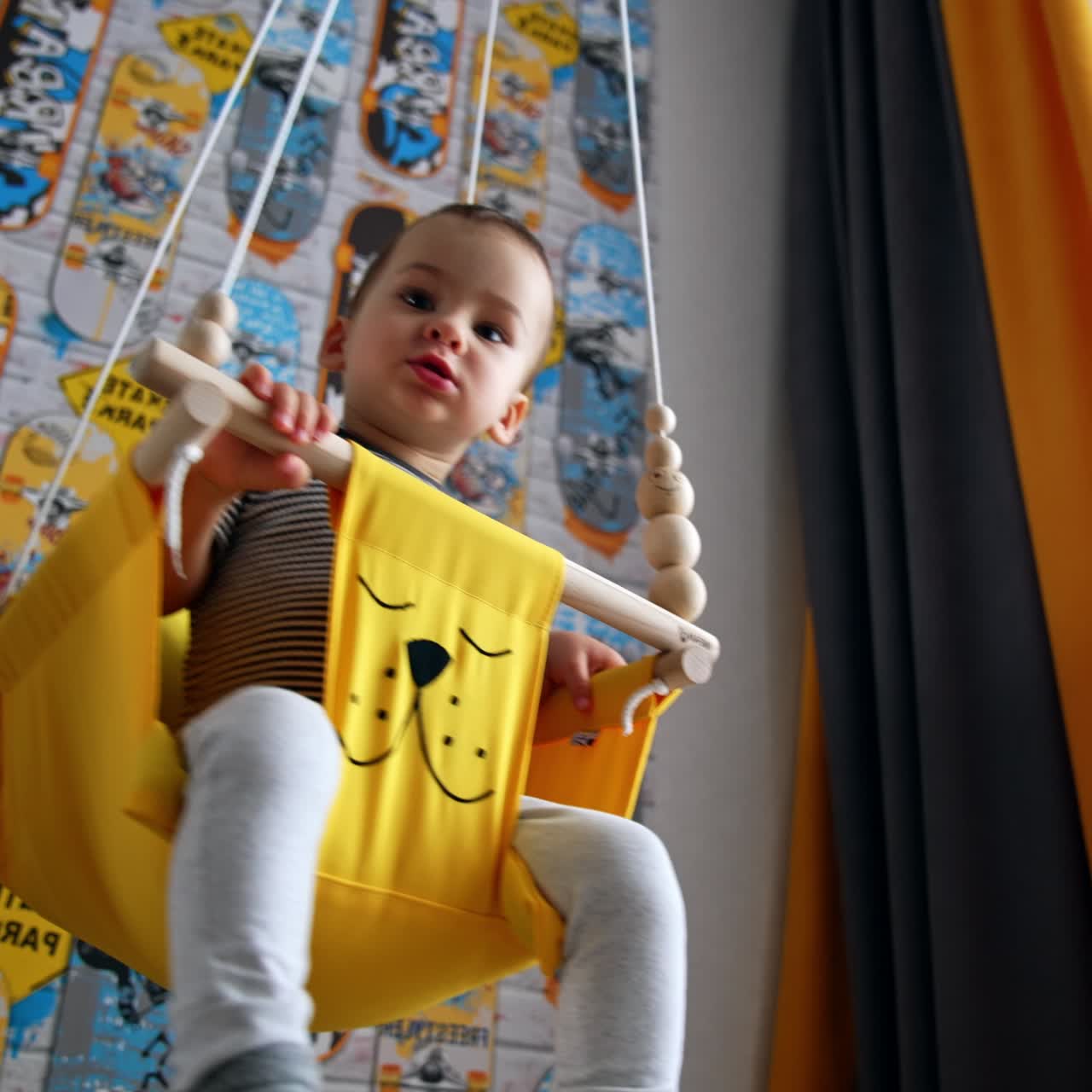 Beautiful kid having fun swinging at home. Baby reaches his hand for something. Low angle view
