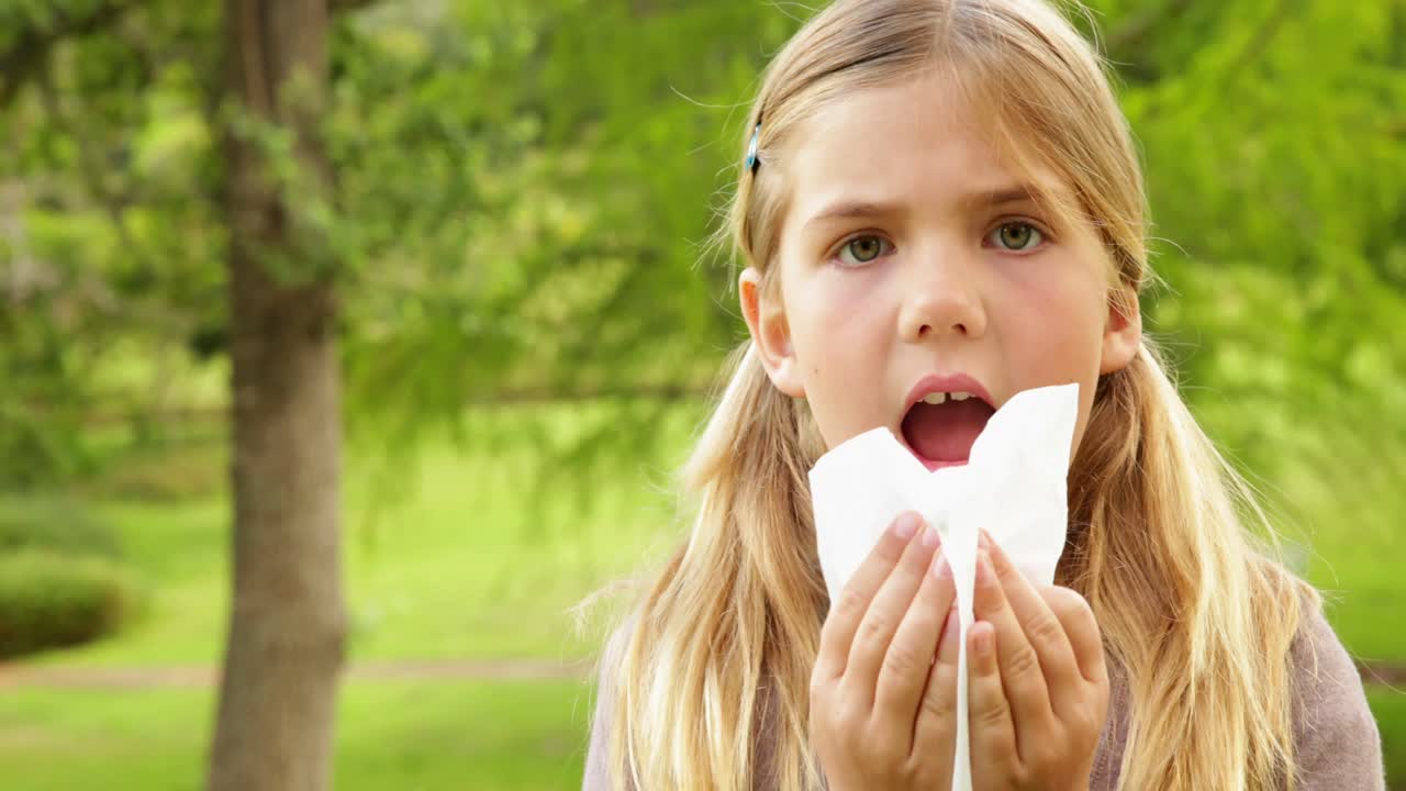 una niña linda soplando la nariz en el parque