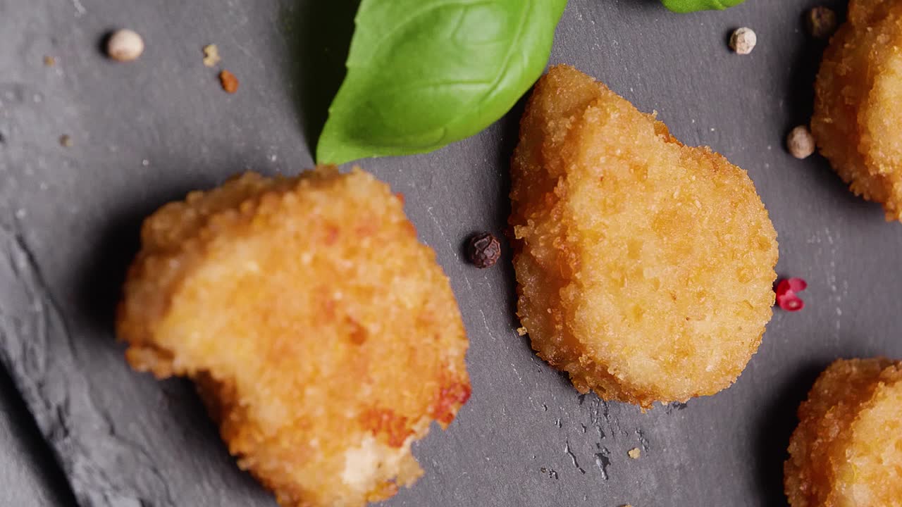 disparo en cámara lenta de nuggets de pollo veganos en una pizarra negra decorada con granos de pimienta y albahaca