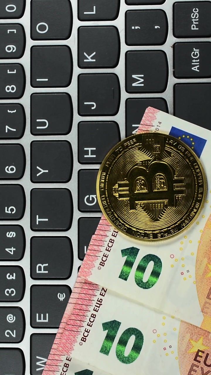 Bitcoin e denaro in Euro su tastiera di computer, vista verticale.