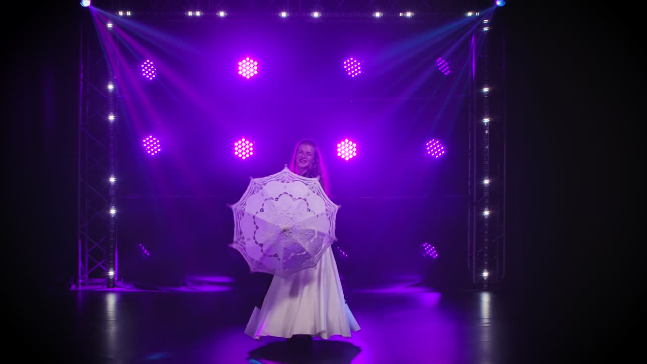 птичьи трюки. женщина вращает кружевный зонтик, на котором сидят белые обученные голуби и ходят по кругу. профессиональное цирковое шоу с птицами в темной студии на фоне фиолетовых огней