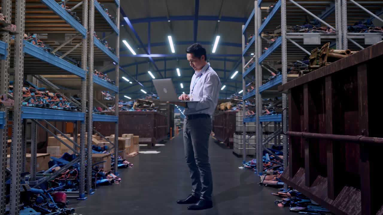 Full Body Side View Of An Asian Male Professional Worker Standing With His Laptop, Industrial Scrap Metal and Recycling Warehouse, Typing On His Laptop'S Keybaord With Meditation