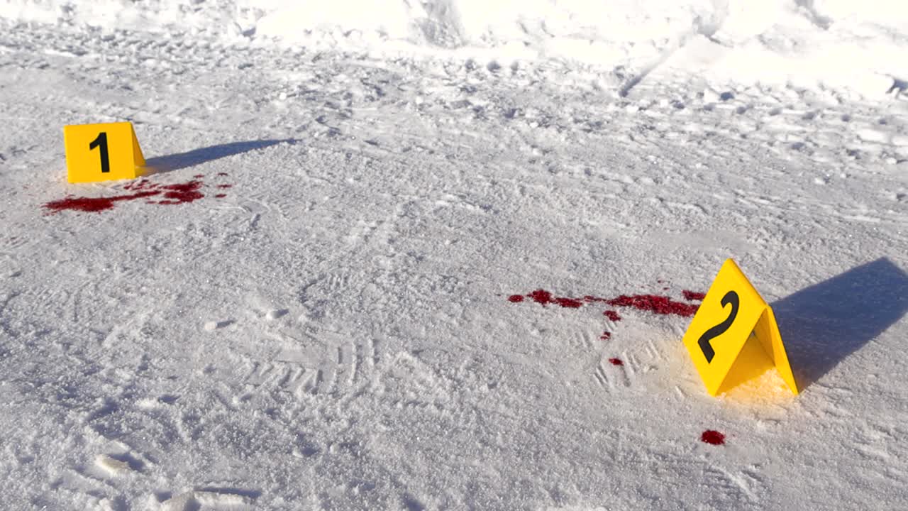 Low angle view of numbered forensic markers placed next to blood puddle documenting violent winter incident with traces across a frozen roadway. Police crime scene investigation on snow covered ground