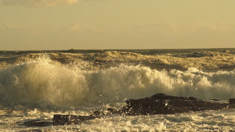 Olas-Del-Mar-Agitadas-Rompiendo-En-La-Costa-Rocosa-Creando-Un-Enorme-Rocío-Durante-La-Puesta-De-Sol-Dorada---Estática-Media