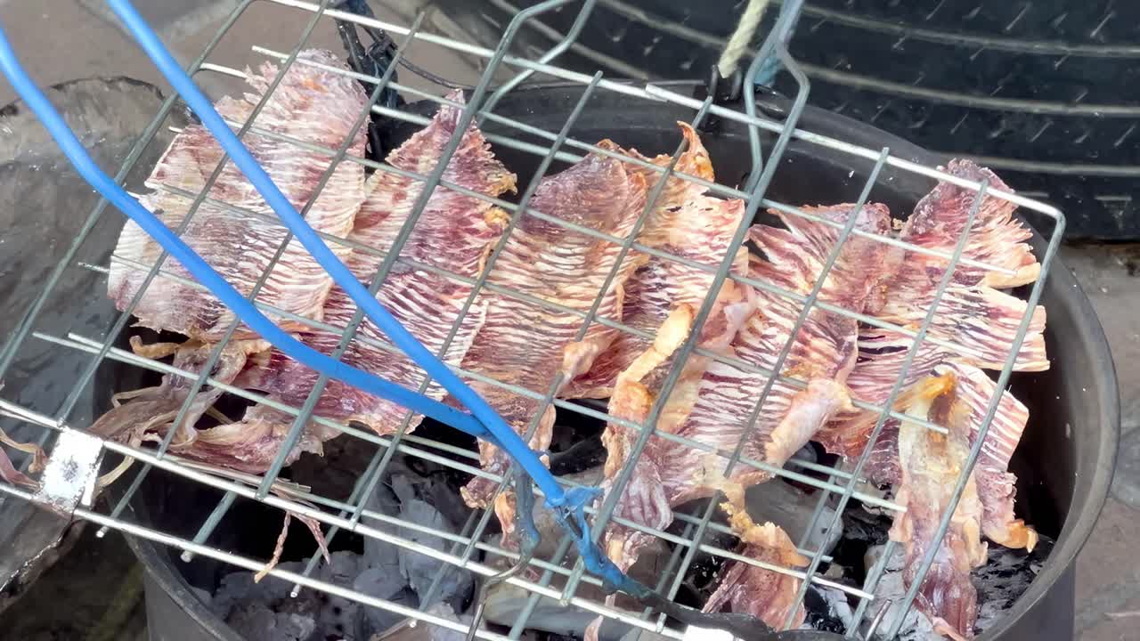 Close-up of fish being grilled over charcoal in a metal basket, highlighting the cooking process.