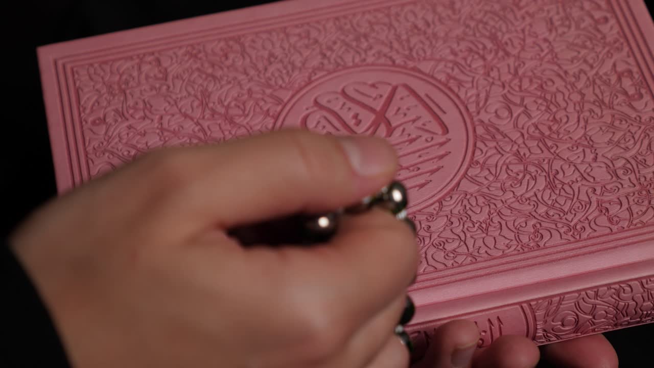 A person doing dhikr on a prayer beads holding a Quran in the other hand