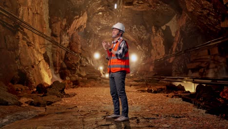 full body side view of asian male engineer with safety helmet smiling and clapping his hands while standing in underground mine tunnel