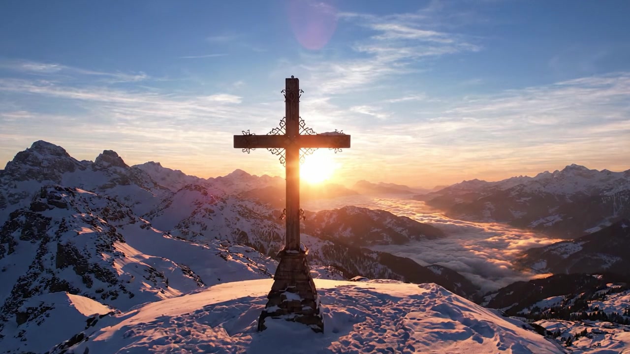 Majestätisches Kreuz auf verschneitem Berggipfel bei Sonnenaufgang: Eine friedliche Szene von Glaube und Natur, eingefangen im frühen Morgenlicht.