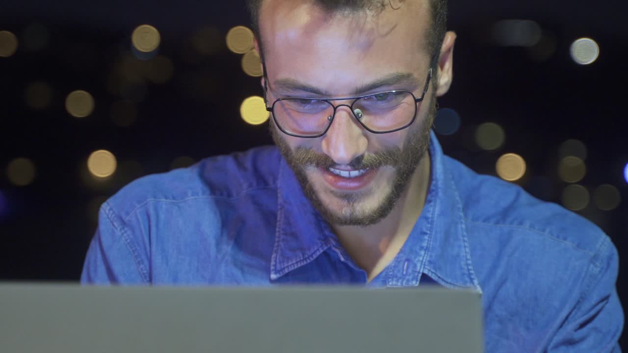 joven feliz trabajando en su computadora portátil junto al mar por la noche.