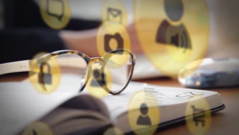 animation of technology icons over, book, glasses and hands of caucasian man typing on keyboard