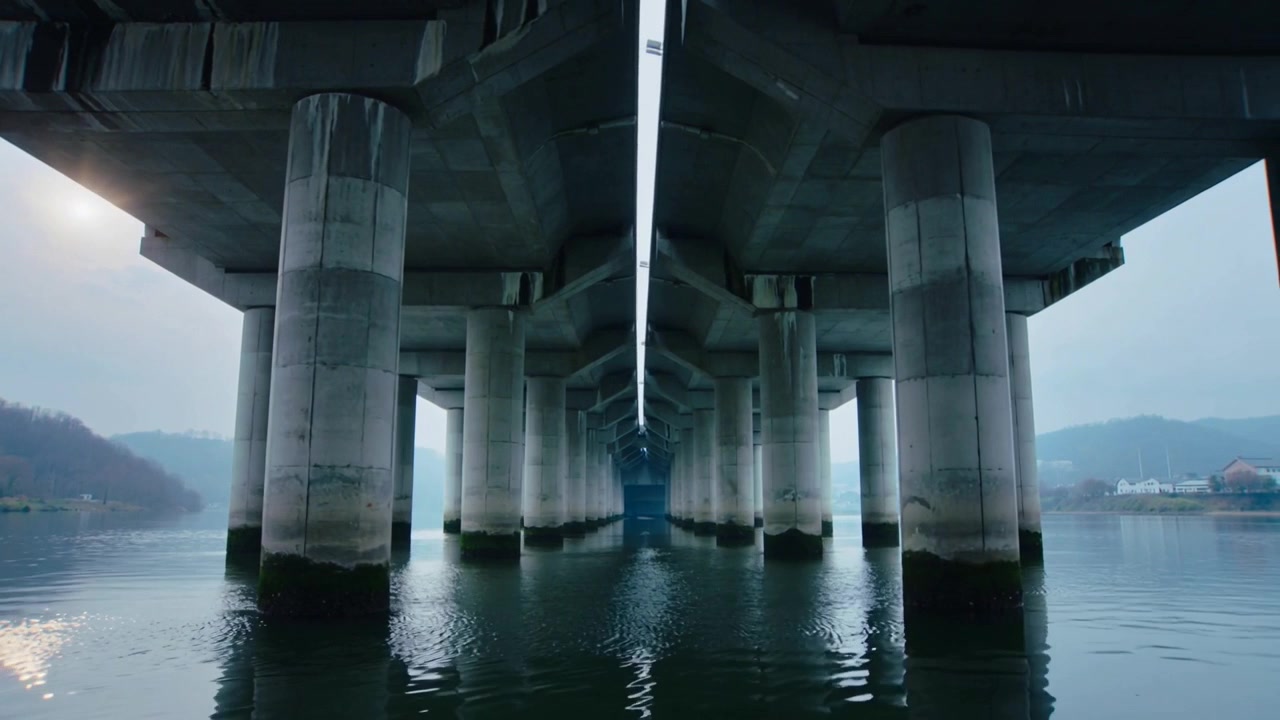 Moving camera approaching vanishing point under concrete bridge, revealing seam, columns, ripples