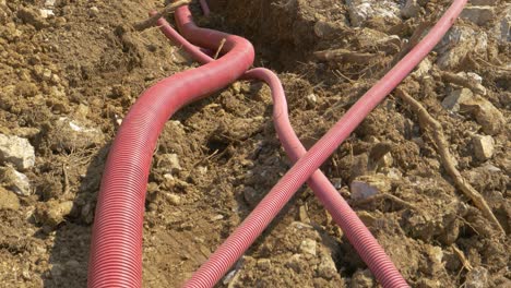 close up: corrugated tubing lies inside a trench near a road under construction.