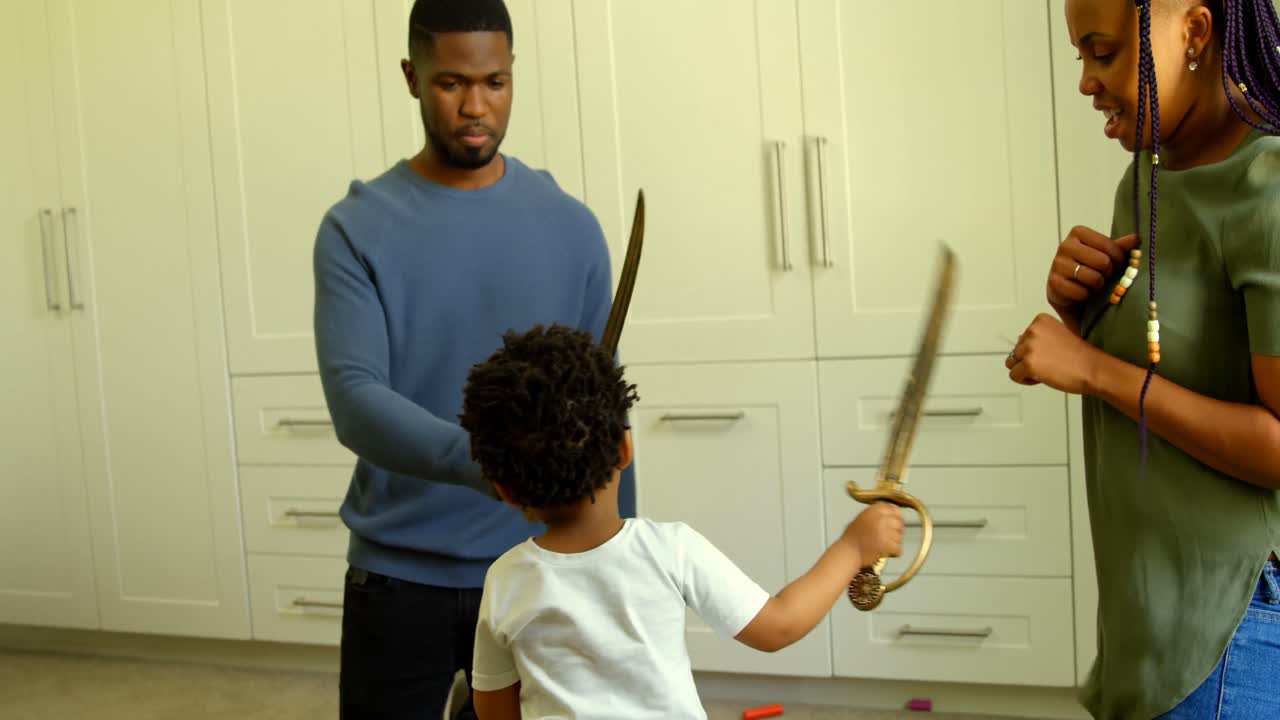 Front view of young black father and son playing with toy sword in a comfortable home 4k