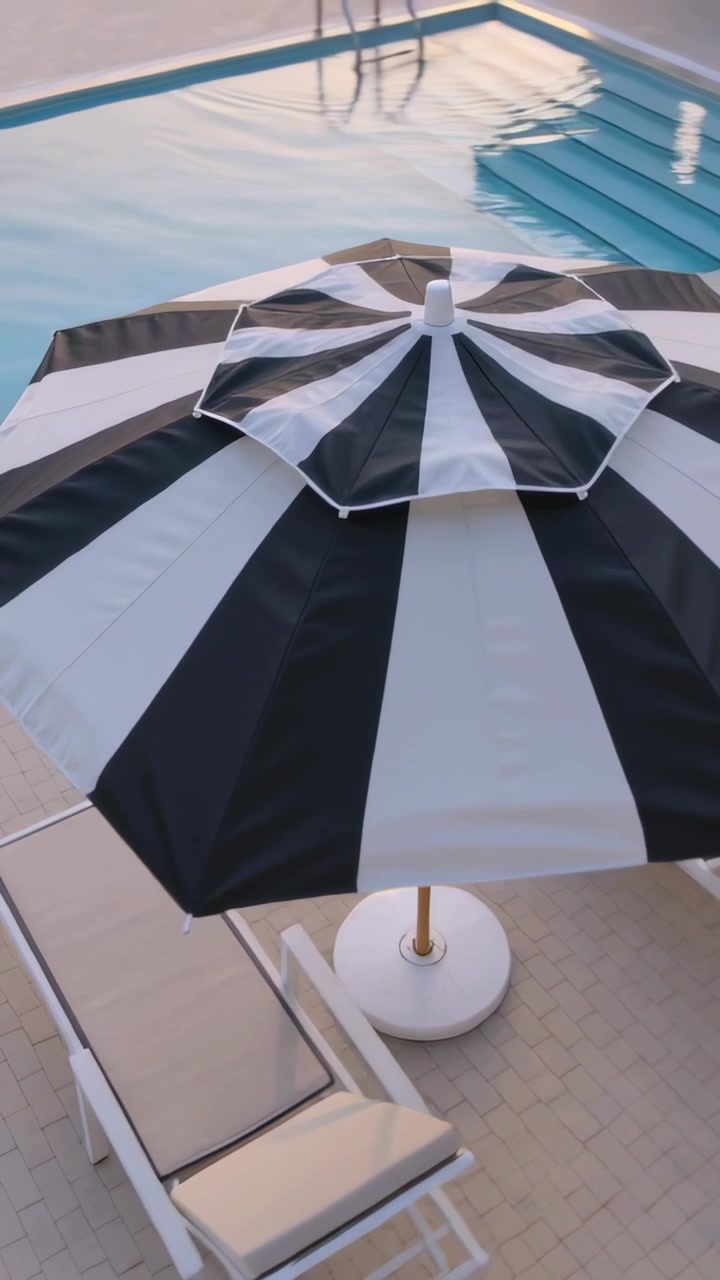Vertical video: Moving camera closing in on striped umbrella at poolside to show canopy and ladder