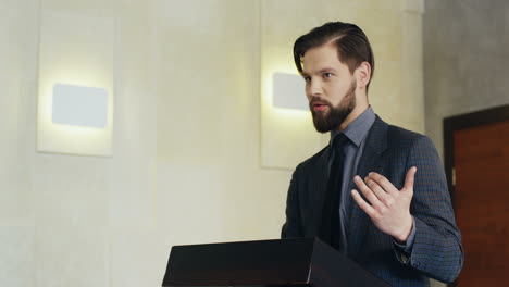 close-up view of caucasian businessman on a podium wearing formal clothes and talking in a conference room