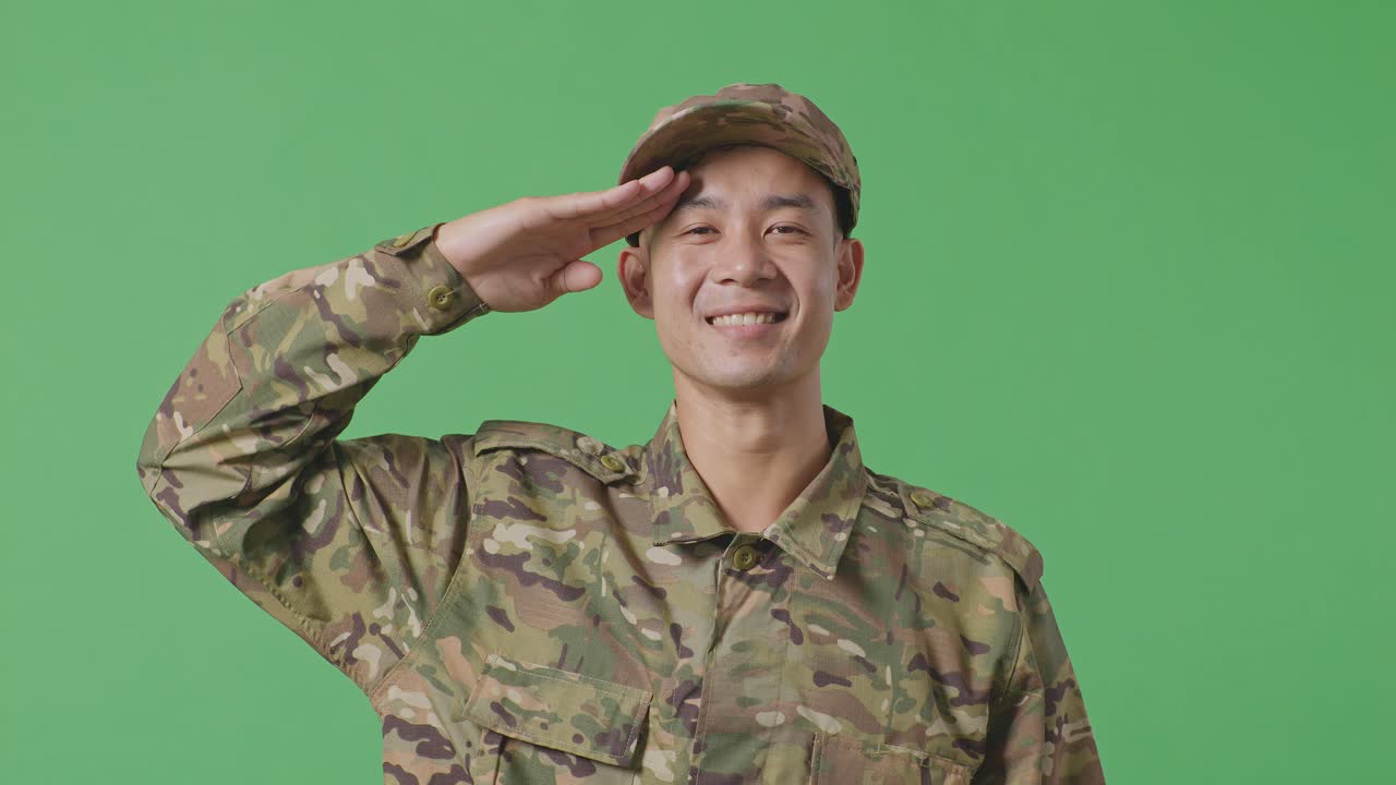 Close Up Of Asian Man Soldier Saluting And Smiling While Standing In The Green Screen Background Studio
