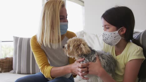madre e hija con máscaras faciales jugando con su perro mascota en casa