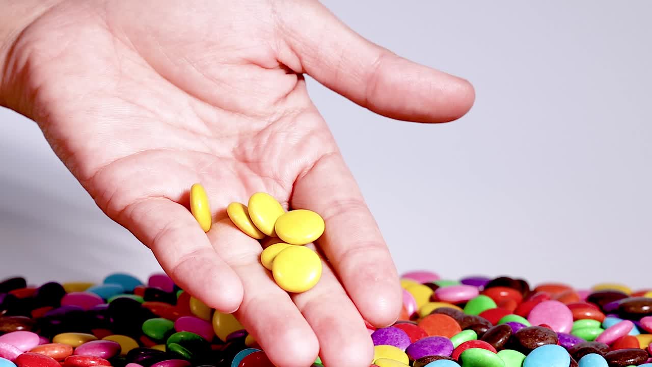 A hand carefully selects and holds yellow candies from a vibrant, multicolored pile.