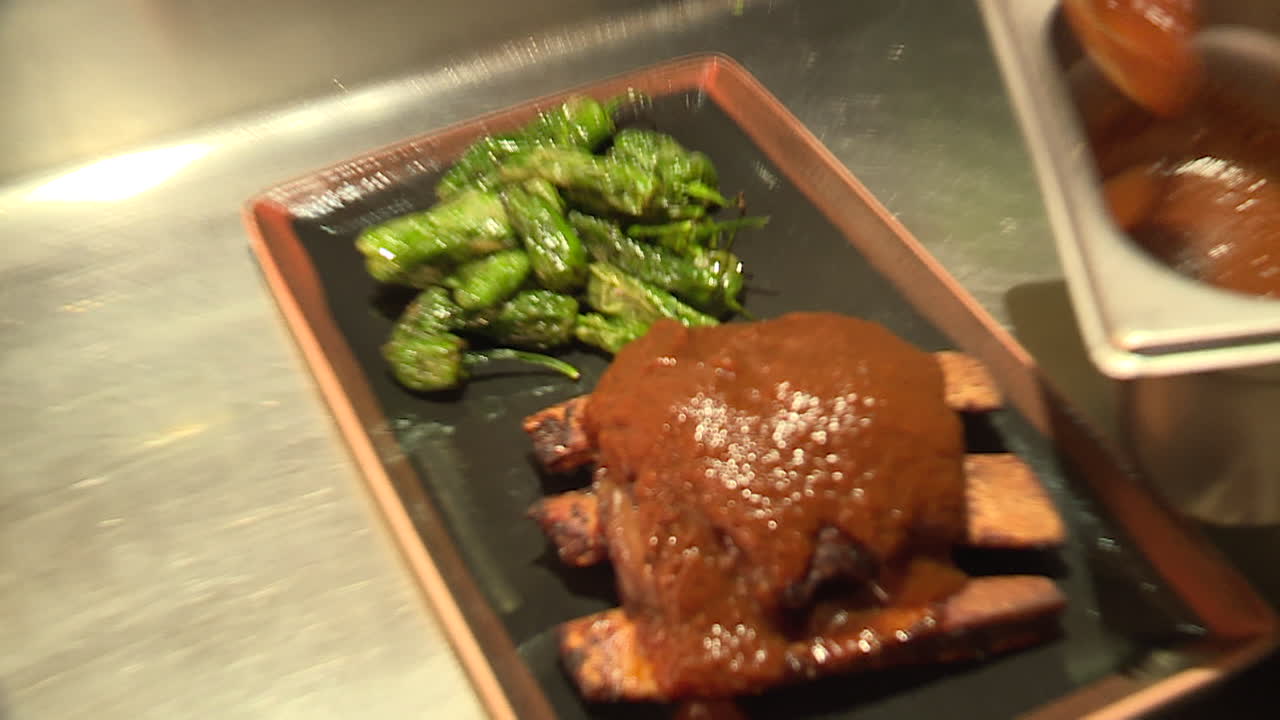 Chef preparing pork ribs with sauce and roasted vegetables