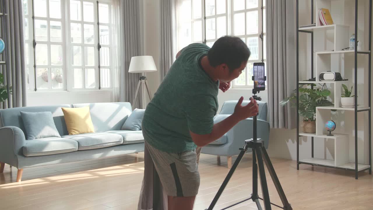 Asian Man Shows Trick With Disappearing On Mobile Phone Camera While Recording On Smartphone Video Content For Social Networks In Cozy Room