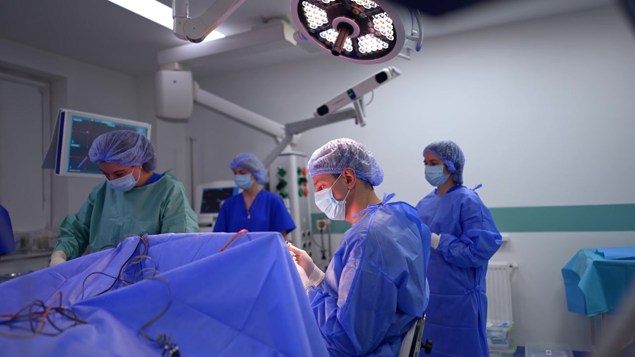 Il chirurgo seduto al tavolo operatorio prende gli strumenti metallici. L'infermiera strumentista prepara gli strumenti sul carrello chirurgico