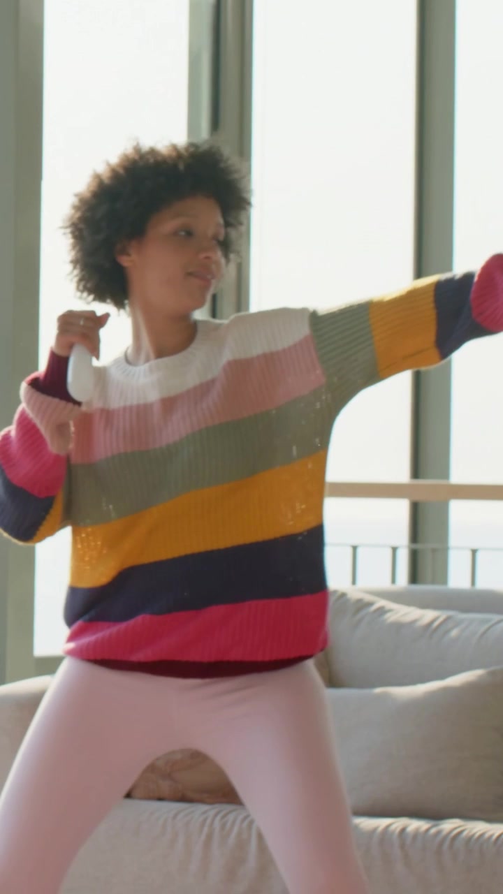 Vertical video: Gesture urging woman singing, dancing at home with mic, striped tee, pink leggings
