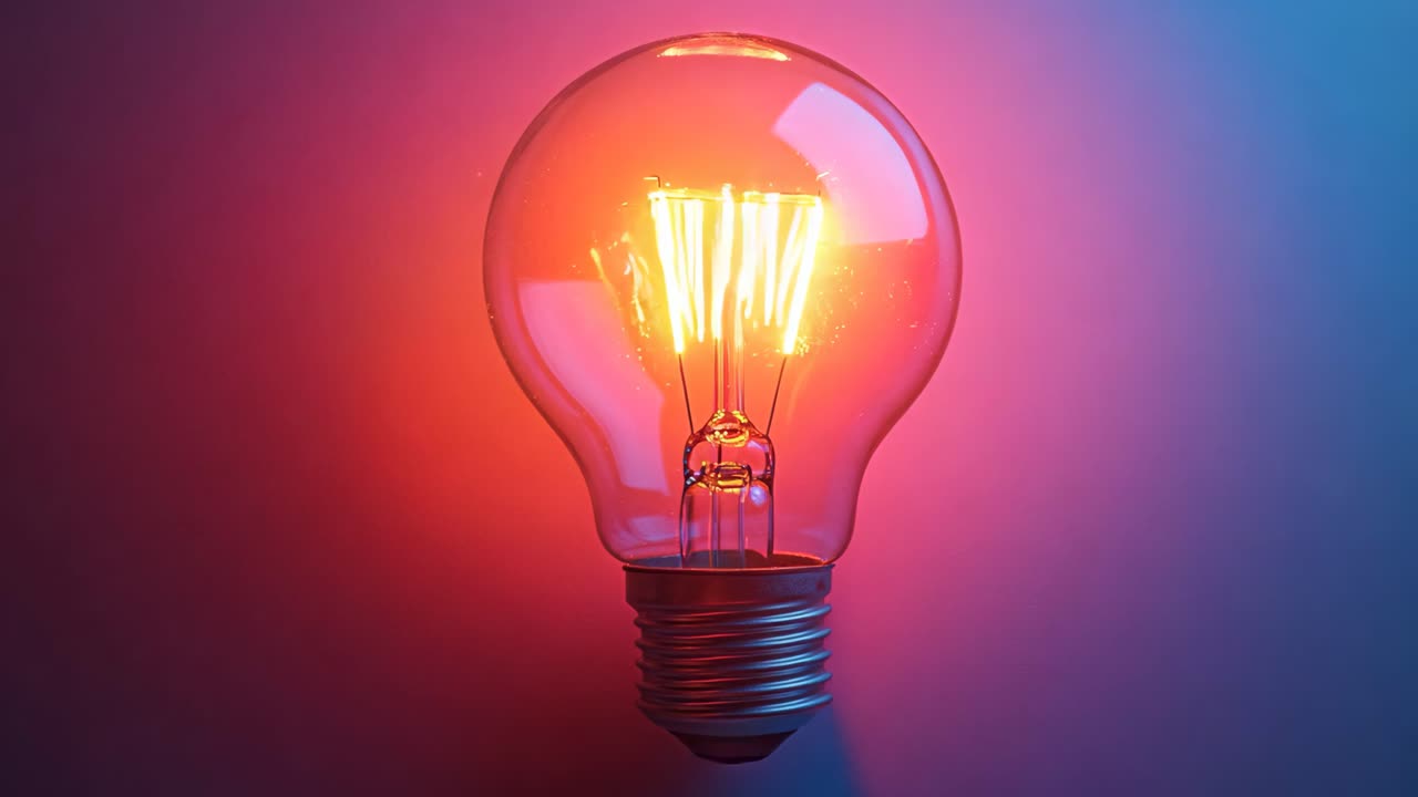 A light bulb is lit up and is sitting on a red background. The light bulb is glowing brightly and is the main focus of the image