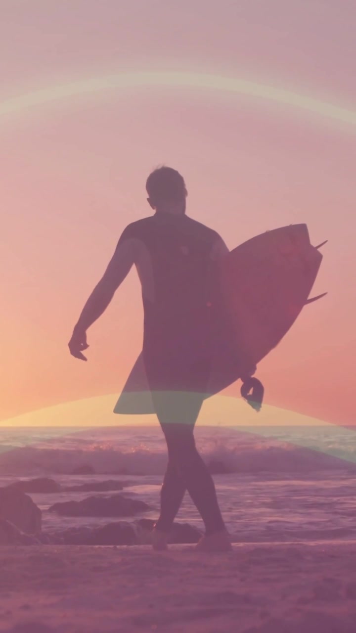 Video vertical: Surfista caminando con traje de neopreno en la playa, sosteniendo la correa de su tabla corta, con el atardecer incitando a entrar al mar.