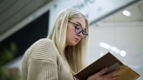 side view of woman in beautiful woven sweater wearing glasses focuses on book, flipping to next page, roof and decorative flower visible behind