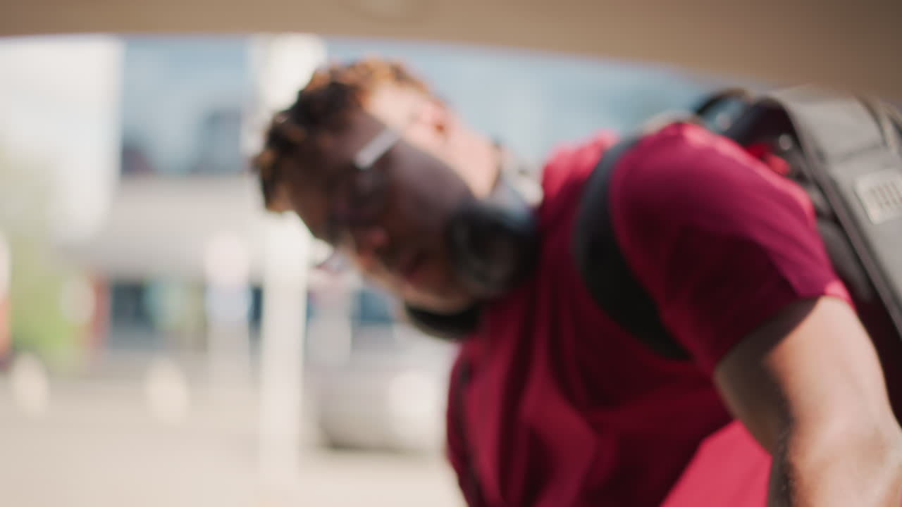 black man loading equipment into trunk outside venue wearing headphones and backpack focused expression shallow depth warm film tones cinematic closeups of windshield interior roof and shoulder shot