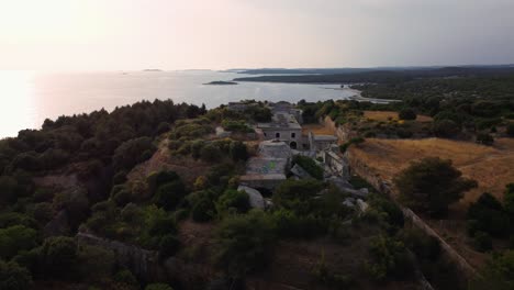 Vista-Aérea-Cinematográfica-Círculo-De-Puesta-De-Sol-De-Drones-Sobre-Una-Fortificación-Histórica-De-La-Primera-Guerra-Mundial-Fortaleza-Junto-Al-Mar-Junto-Al-Idílico-Mar-Mediterráneo-Adriático-Con-Agua-Azul-Y-Playas-Escondidas-En-Verano