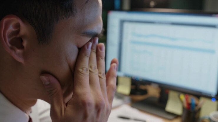 Staring at dual monitors, man at desk in shirt tie rubbing, leaning, resuming review, copy space