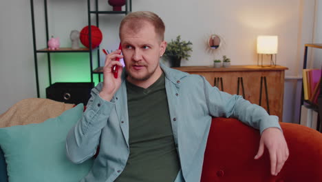 Adult-caucasian-man-enjoying-talking-on-mobile-phone,-conversation-with-friends-at-home-on-couch