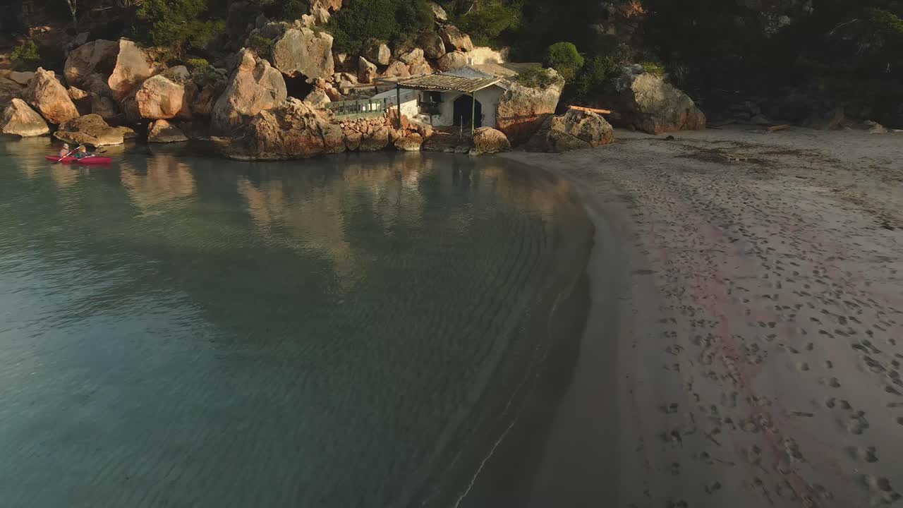 casa aislada en la playa construida en rocas con residentes recorriendo la propiedad en kayak