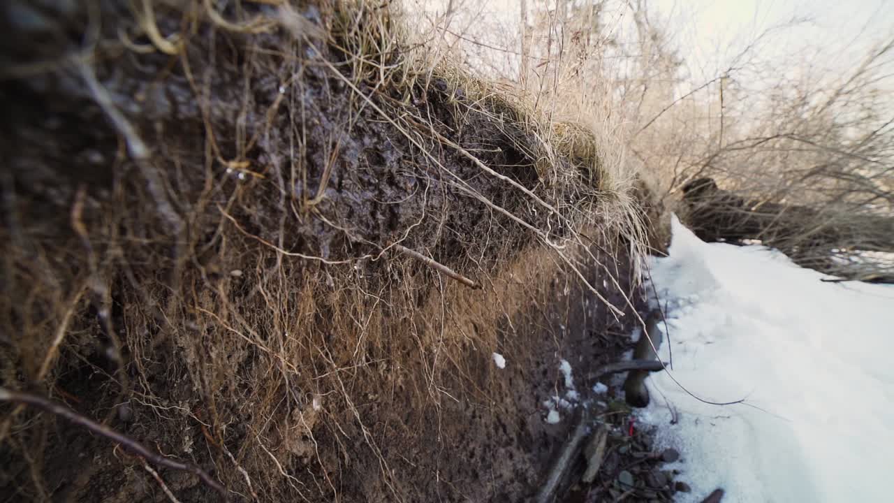 Neve che si scioglie gocciola attraverso la terra al rallentatore sul bordo di una spiaggia di ciottoli.