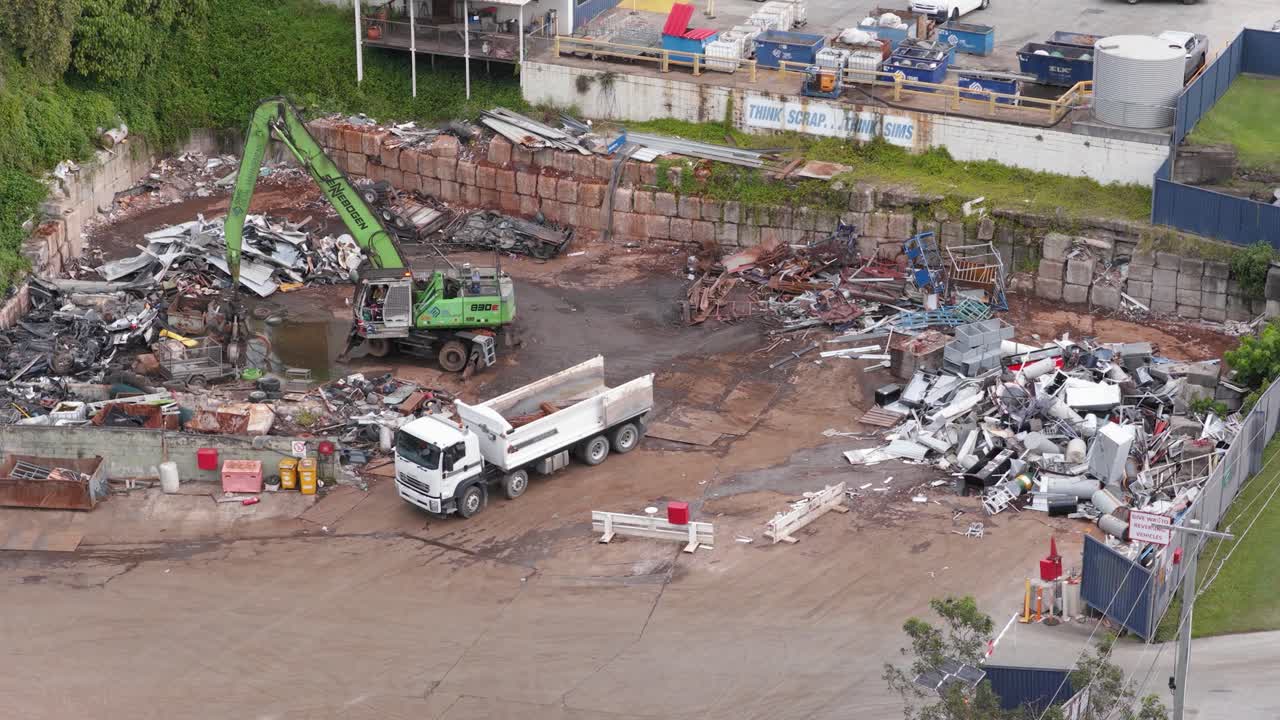 Drone footage captures a truck and machinery sorting metal scrap in a Gold Coast junkyard under daylight