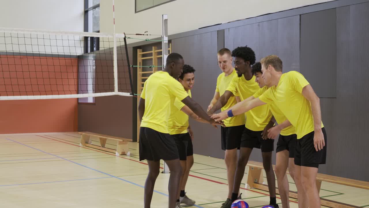 Hombres diversos de amarillo observan a un entrenador arrodillado dando indicaciones, formando un corrillo en el gimnasio con balones para la estrategia